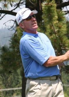 A mustachioed man wearing a white baseball cap and light-blue polo shirt looking to the right of the image