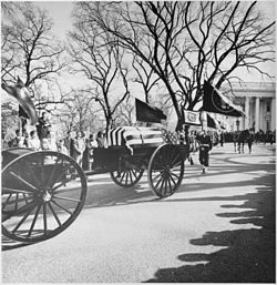 A limbers and caissons bearing the casket of U.S President John F. Kennedy seen moving down the White House drive on the way to St. Matthew's Cathedral on November 25, 1963. A color guard holding the presidential colors, the flag of the president of the United States, and the riderless horse "Black Jack", follow behind. Photograph of the caisson bearing the flag-draped casket of President John F. Kennedy leaving the White House... - NARA - 200455.jpg