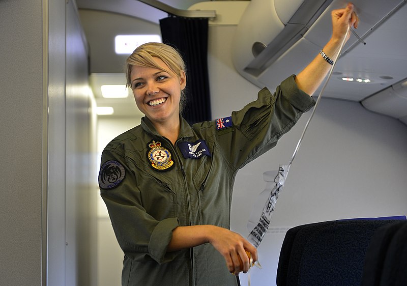 An aircraftswoman wearing a uniform is giving a safety briefing onboard an aircraft.