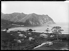 Schwarz-Weiß-Bild einer weitläufigen Bucht mit kleinen Holzhäusern und Hügeln im Hintergrund