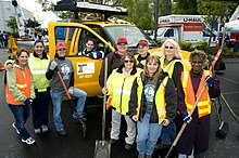 A group of female workers holding shovels stand in front of a yellow truck at the Women in Trades Fair at Seattle Center.