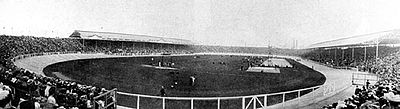 photographie en noir et blanc d'un stade entouré de tribunes, une piste d’athlétisme entoure la pelouse