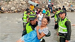 Wenezuelscy migranci przekraczający rzekę, wspomagani przez kolumbijską policję