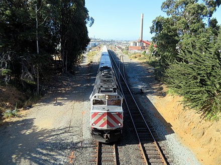 A southbound train passing the proposed station site (June 2018); the Quint Street Lead can be seen branching east from the northbound mainline.