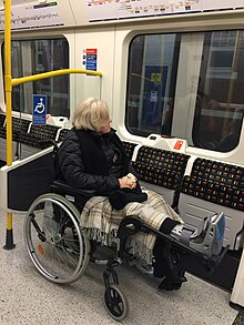 Uma fotografia de uma pessoa em cadeira de rodas estacionada no espaço reservado dentro de um trem de metrô.