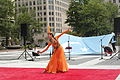 Uyghur woman dancing in front of a large Kökbayraq in Washington D.C.