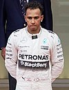 Lewis Hamilton in silver racing overalls standing on the third spot on the podium