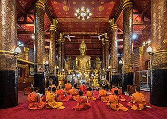 Bhikshus assis devant une statue de Bouddha dorée pendant l'heure de la prière à l'intérieur du Wat Mai Suwannaphumaham, temple bouddhiste du 18e siècle, devant une statue de Bouddha dorée, à Luang Prabang. Septembre 2023.