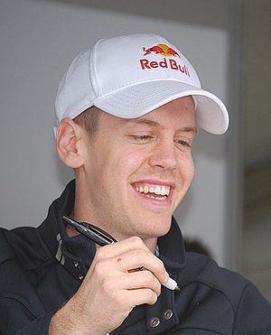 Sebastian Vettel signs an autograph while wearing a hat