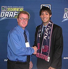 New England selected Clint Dempsey 8th overall. The 2004 MLS Rookie of the Year is a 4x MLS All-Star, 3x U.S. Soccer Player of the Year, and the 2017 MLS Comeback Player of the Year. He earned 141 caps with he US Men's National Team, representing the United States at the 2006, 2010, and 2014 FIFA World Cup. With 57 goals, he and Landon Donovan are tied for most goals for the USMNT. He was elected to the National Soccer Hall of Fame in 2022. Steve Nicol and Clint Dempsey at the 2005 MLS SuperDraft.jpg