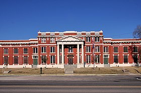 Vue de la façade d'un bâtiment en briques rouges. À l'entrée des colonnes blanches soutiennent un fronton.