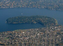 Una península boscosa rodeada por un lago y barrios urbanos.