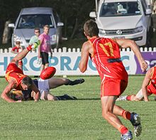Player (foreground) moving in to collect the crumb from a contest Australian rules football action.jpg