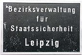 Schwarze geriffelte Metalltafel mit weißen Buchstaben, die in vier Zeilen mittig zentriert jeweils ein Wort zeigen „Bezirksverwaltung für Staatssicherheit Leipzig“