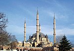Large mosque with four minarets and a large dome of dark stone.