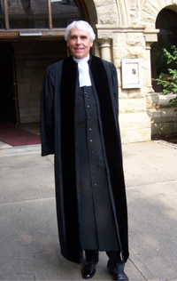 A traditional open-front Geneva gown worn over a cassock with white preaching tabs. Geneva gown.png