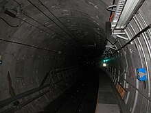 Circular concrete tunnel with cables running along the walls and a narrow emergency walkway on the right