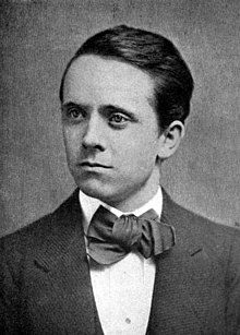 black and white portrait of white man with dark hair, wearing a suit and bow-tie