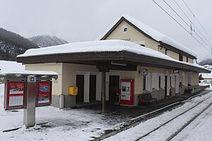 Zweistöckiges Gebäude mit Satteldach neben Plattformen und Gleisen