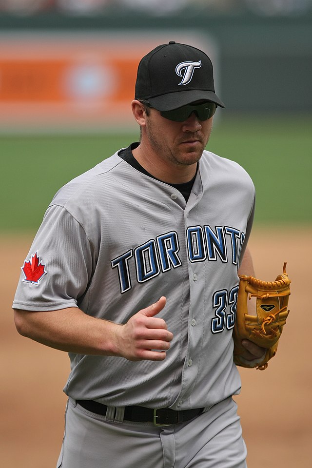 A man wearing a gray baseball uniform with "Toronto" across the chest and a black baseball cap