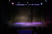 A dark proscenium stage illuminated by the glow of purple lights