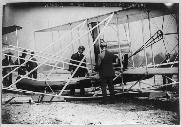 Wilbur Wright (back to camera) and mechanic Charlie Taylor fix a canoe to the Wright A Flyer used during the Celebration.