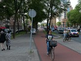 Young woman is cycling over the bike path along the car traffic on the road Weesperpstraat; free photo Amsterdam, Fons Heijnsbroek, July 2022