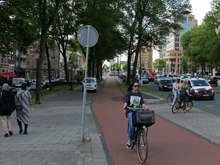 A cycle path in Amsterdam. The Dutch are well-known for having an extensive network of cycle tracks (fietspad
). Young woman is cycling over the bike path along the car traffic on the road Weesperpstraat; free photo Amsterdam, Fons Heijnsbroek, July 2022.tif