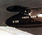 A close-up of a jet in flight, the pilot is wearing a white helmet. On the nose of the plane are the Spanish words "Fuerza Aerea Argentina" and the designation code "B-108".