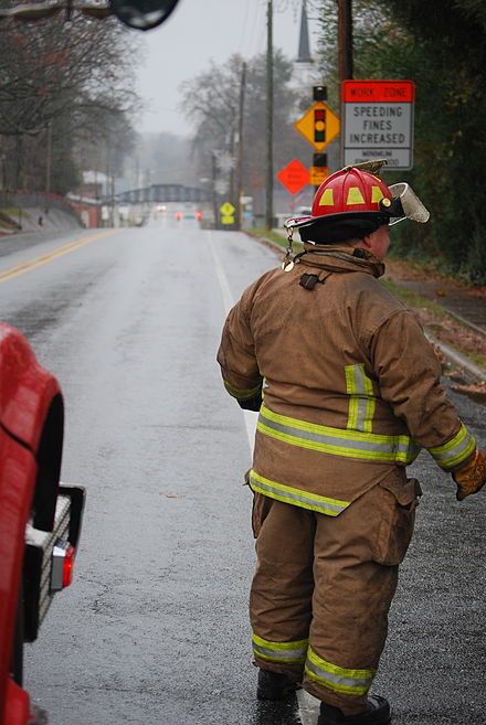 A volunteer firefighter stands to the edge of a road.