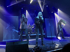 Quatre membres d'un groupe de rock, comprenant trois hommes et une femme, jouant sur scène