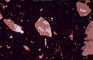 Microscopic photo of a laterite thin section (length 1,25 mm) shows quartz relics (white) in voids of a ferrugineous matrix.