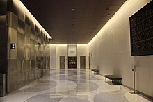 Lobby corridor north of the elevators. The floor has wavy white and gray pavers, and the left wall has a textured pattern on a metal surface.