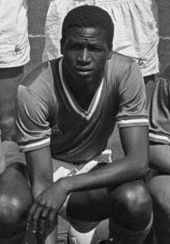 Photo noir et blanc d'un footballeur accroupi, la main droite à terre et le bras gauche en appui sur le genou