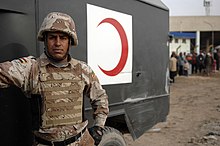 An Iraqi Ground Forces medic next to his military ambulance featuring a red crescent emblem An Iraqi medic from 2nd Brigade, 9th Iraqi Army (Mechanized), stands by his ambulance outside the Taji Sports Complex.jpg