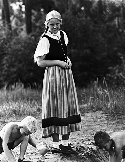 A young German girl in dirndl watching boys playing.
