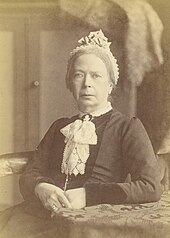 Photographie sépia d'une femme assise en robe victorienne conservatrice