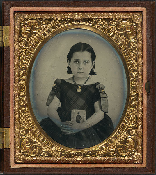 Girl in a mourning dress holding a framed photograph of her father, who presumably died during the American Civil War