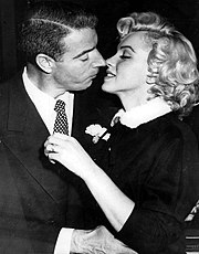 Nahaufnahme des Küssens von Monroe und DiMaggio;Sie trägt einen dunklen Anzug mit weißem Pelzkragen und er einen dunklen Anzug