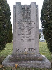 Large upright grey granite stone engraved with the name Mulqueen at the bottom, an Irish Cross at the top, names of family members in the middle.