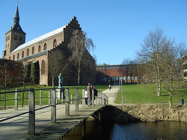 St. Canute's Cathedral seen from Eventyrhaven park. The statue represents Hans Christian Andersen. The yellow building stands on the site of the forme