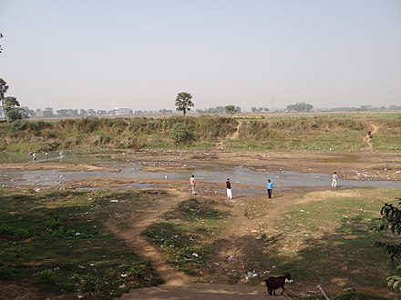 A small river's valley in India shows extensive littering of plastic and paper. Human waste, illustrated by the urinating man, increase fecal coliform and other bacteria levels in the water.