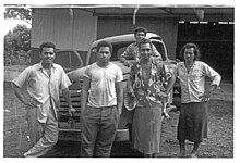 Photo en noir et blanc montrant 5 jeunes hommes polynésiens posant devant une voiture