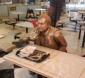 A brass statue of a man eating a hamburger in ...
