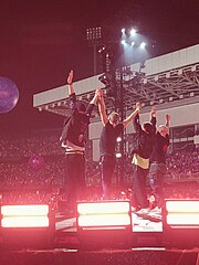 Four men holding each other's hands raise their arms to thank their audience