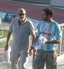 Maurizio Felugo ist auf der Tribüne eines Stadions zu sehen, im Hintergrund ist eine Laufbbahn und eine Eckfahne erkennbar. Felugo trägt ein Hemd mit blau-weißen Längsstreifen und der Nummer 6 auf der Brust, dazu eine Tarnfarben-Hose. Pietro Figlioli ist während eines Spiels im Wasser, er trägt eine blaue Bademütze mit der weißen Nummer 4.