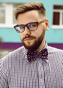 Мужчина в классическом хипстерском образе: борода, очки, клетчатая рубашка, бабочка.