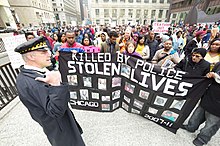 A Chicago Police Department officer in front of protestors during a protest over the killing of Trayvon Martin, part of Occupy Chicago, in 2012 Occupy Chicago protestors (13).jpg