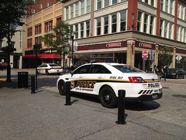 Two Pittsburgh Police vehicles parked at Market Square. In the foreground, a Ford Taurus Police Interceptor with the fleet's new livery, while in the background is a Chevrolet Impala displaying the Bureau's old livery.