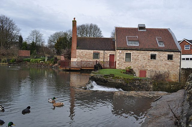 Water flowing over the dam with renovated former mill building in Old Pleasley village